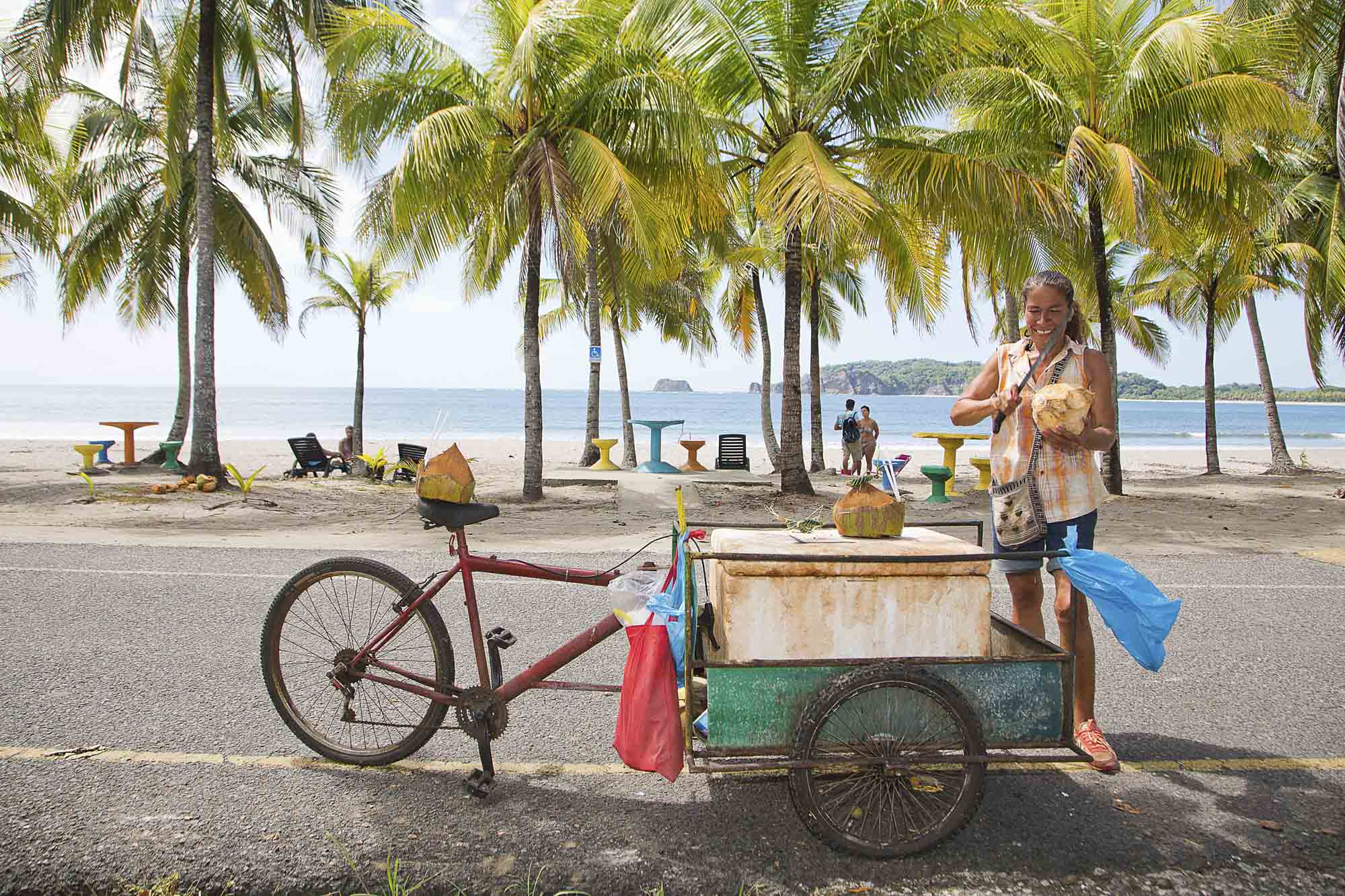 Costa Rica, Provinz Guanacaste, Samara, Playa Carillo, ambulante Händlerin verkauft Kokosnussmilch, zwischen Palmen am Strand